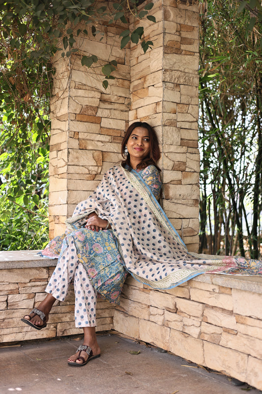 Woman in a patterned outfit standing against a stone wall with greenery in the background